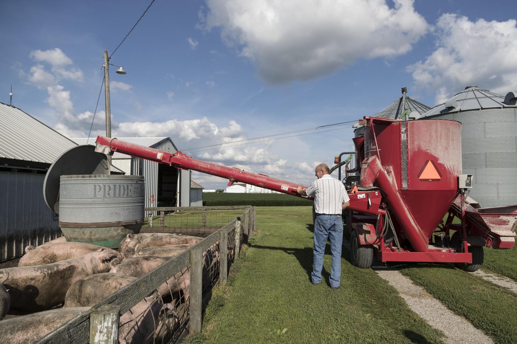 A farmer at work beside a red feed mixer on a hog farm in Benton County, Iowa